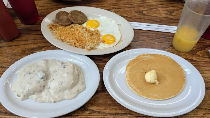 Three breakfast plates at Roxanne's Cafe — biscuits and gravy, eggs with sausage patties and hashbrowns, and a hotcake